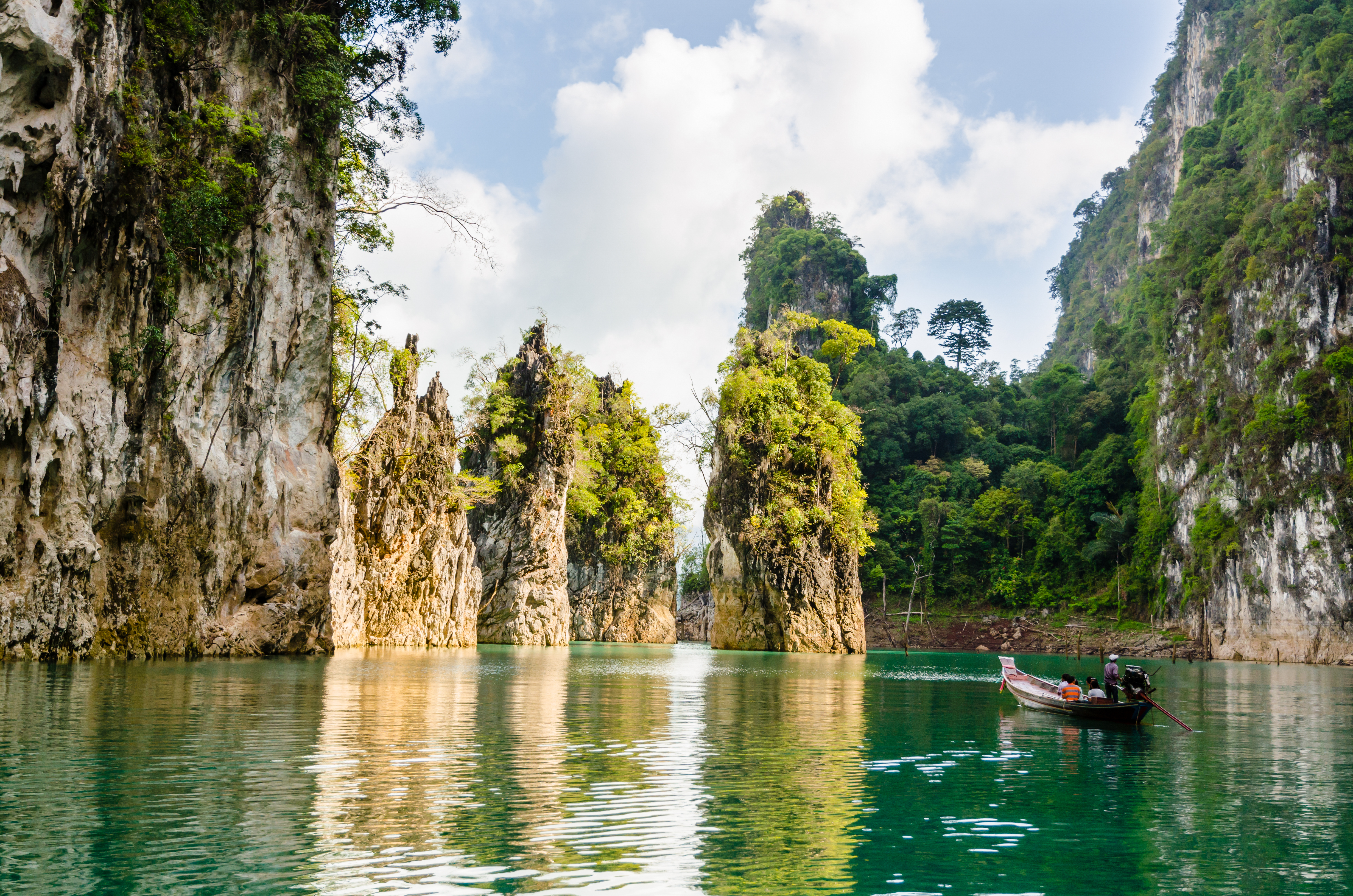Scenic limestone cliffs and boat gliding through turquoise water in Khao Sok National Park