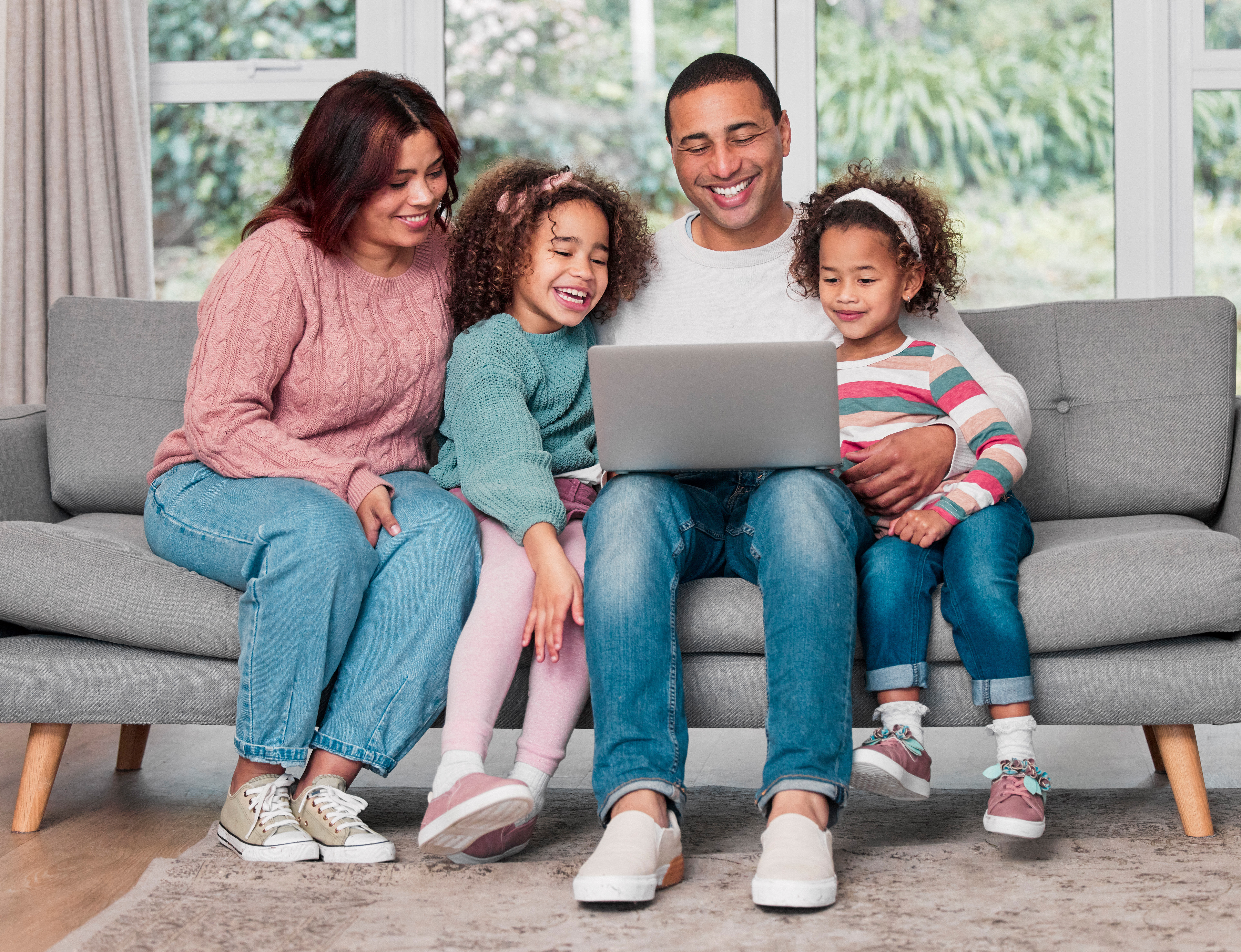 Happy family sitting on sofa, gathered around a laptop for learning or leisure
