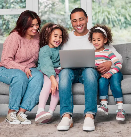 Happy family sitting on sofa, gathered around a laptop for learning or leisure