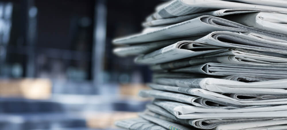 A pile of newspapers stacked on a desk.