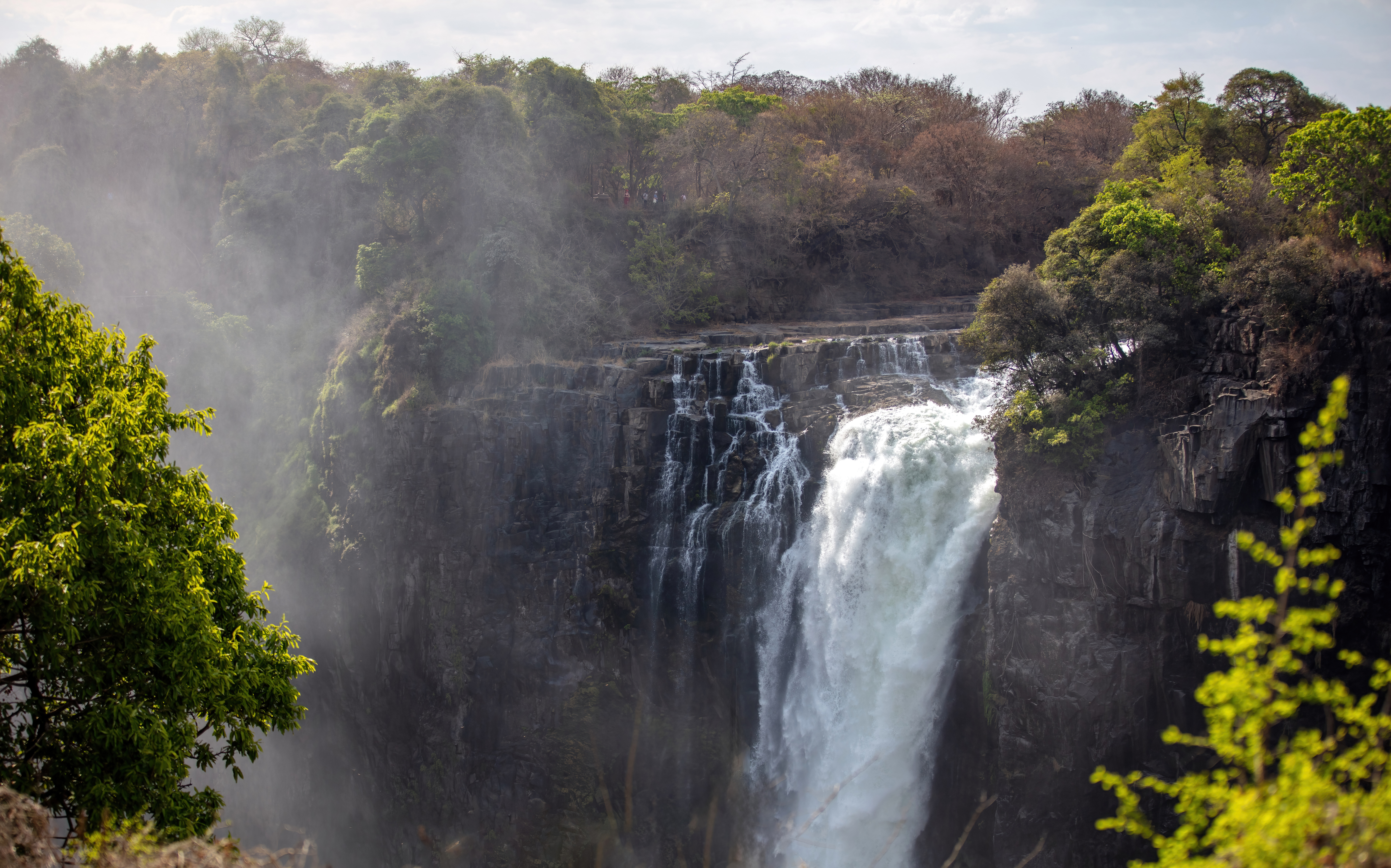Misty waterfall cascading over rocky cliffs surrounded by lush greenery in Zambia