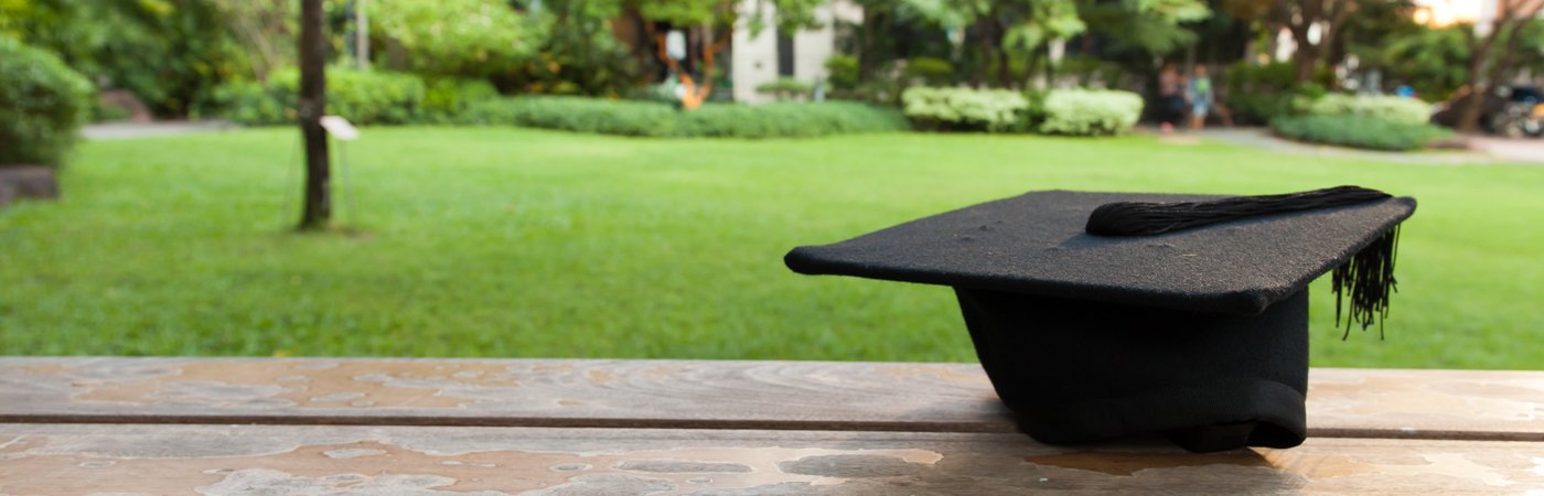 Black graduation cap resting on a wooden bench in a peaceful garden setting.
