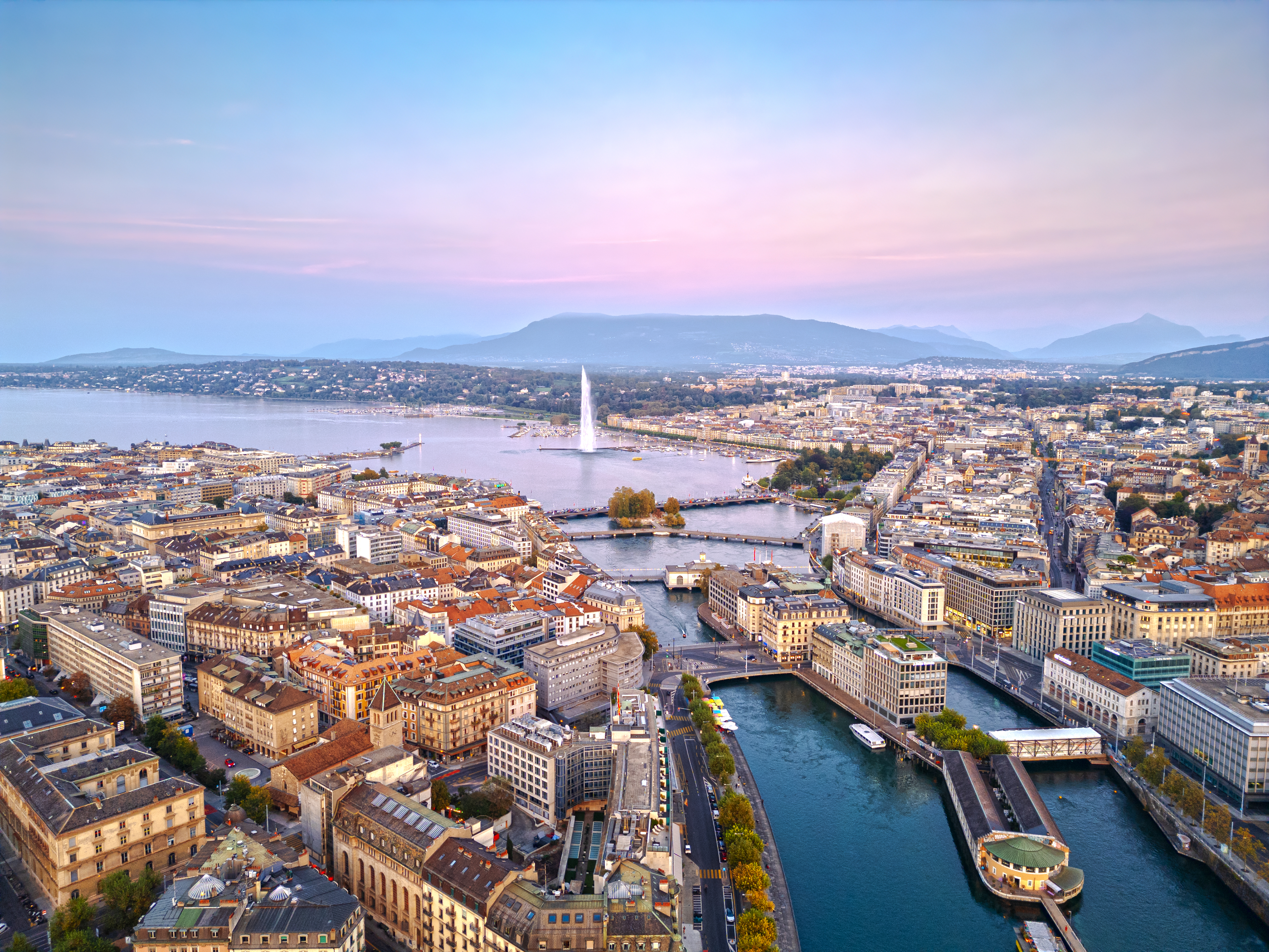 Twilight cityscape of Geneva with Jet d’Eau fountain and mountains in the background