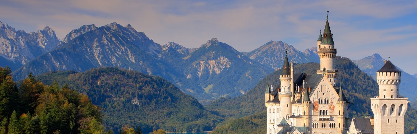 Neuschwanstein Castle set against a backdrop of alpine mountains and forests in Bavaria, Germany.