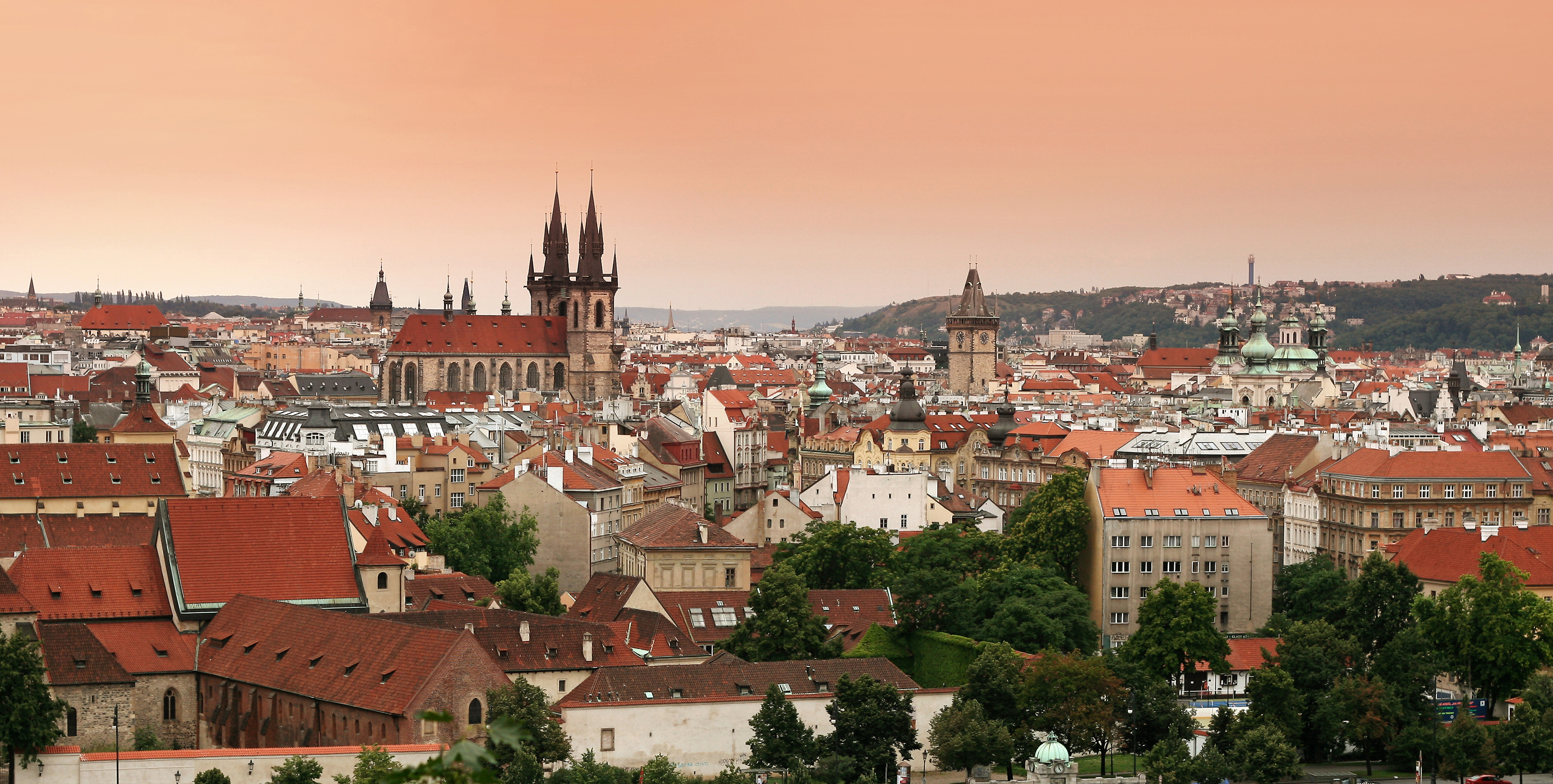 Prague cityscape with red rooftops and gothic church spires under a peach-coloured sky
