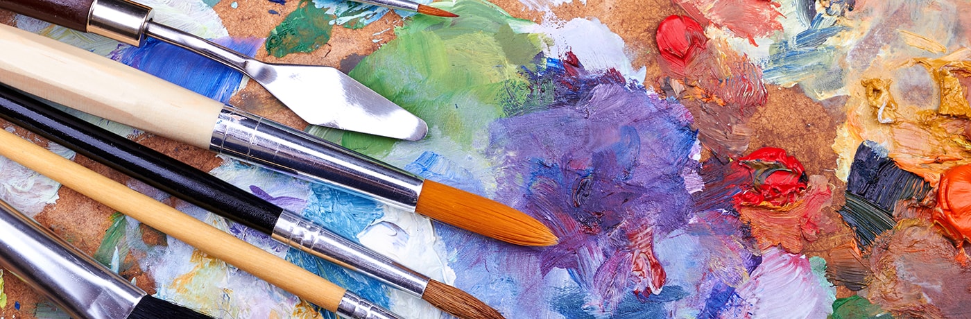A range of colours painted on a canvas with a variety of artistic tools on top. 