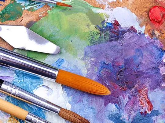 A range of colours painted on a canvas with a variety of artistic tools on top.