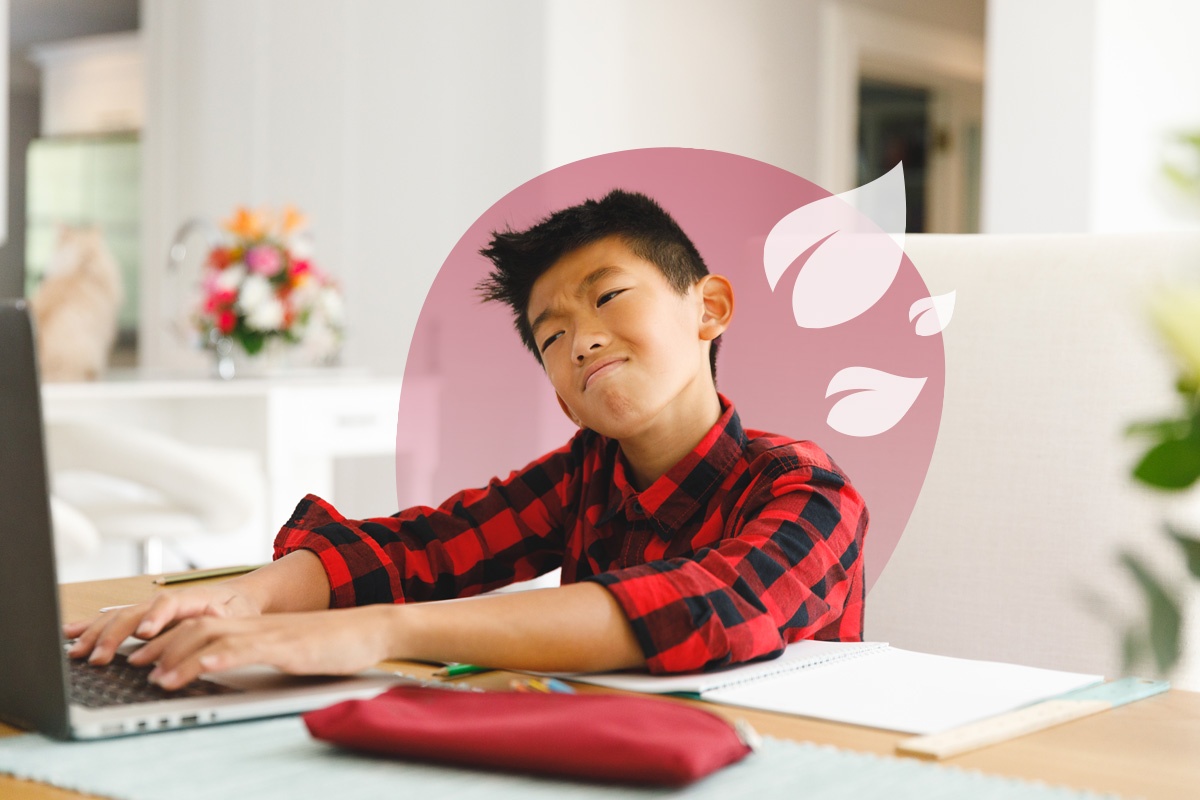A young student with a pensive expression, typing on a laptop at a desk with an open notebook.