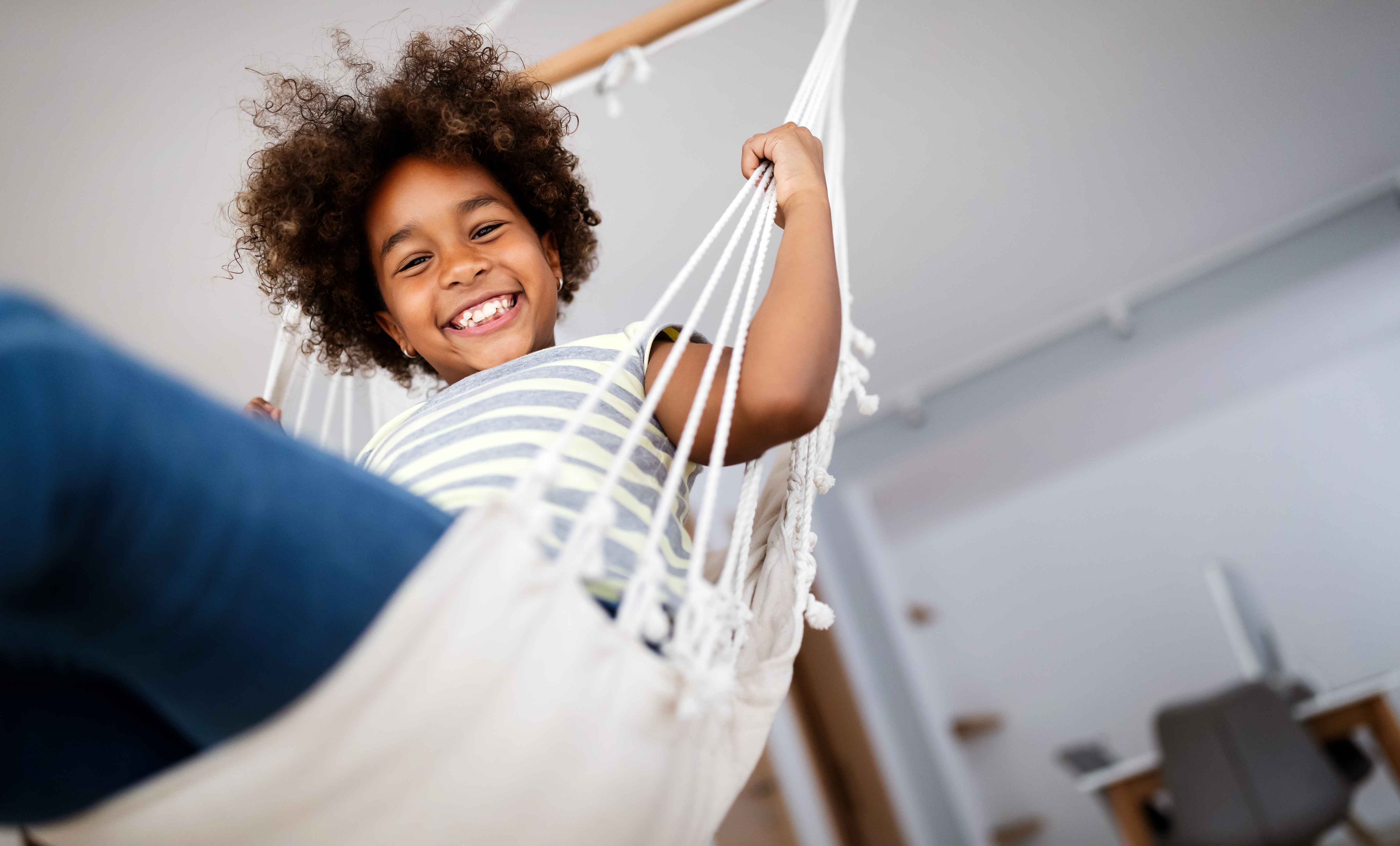 Happy child relaxing in a hammock at home, smiling confidently at the camera.