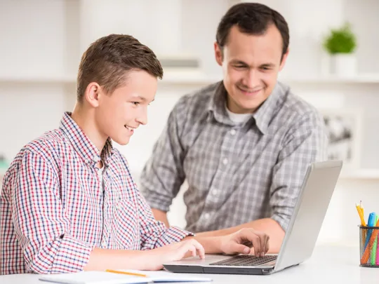 Parent supporting teenage son with online learning at home, highlighting personalised homeschooling support