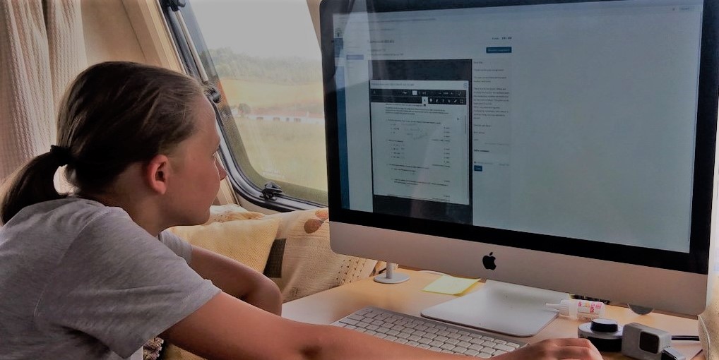 Learner engaging with online coursework on a desktop computer in a well-lit caravan setting.
