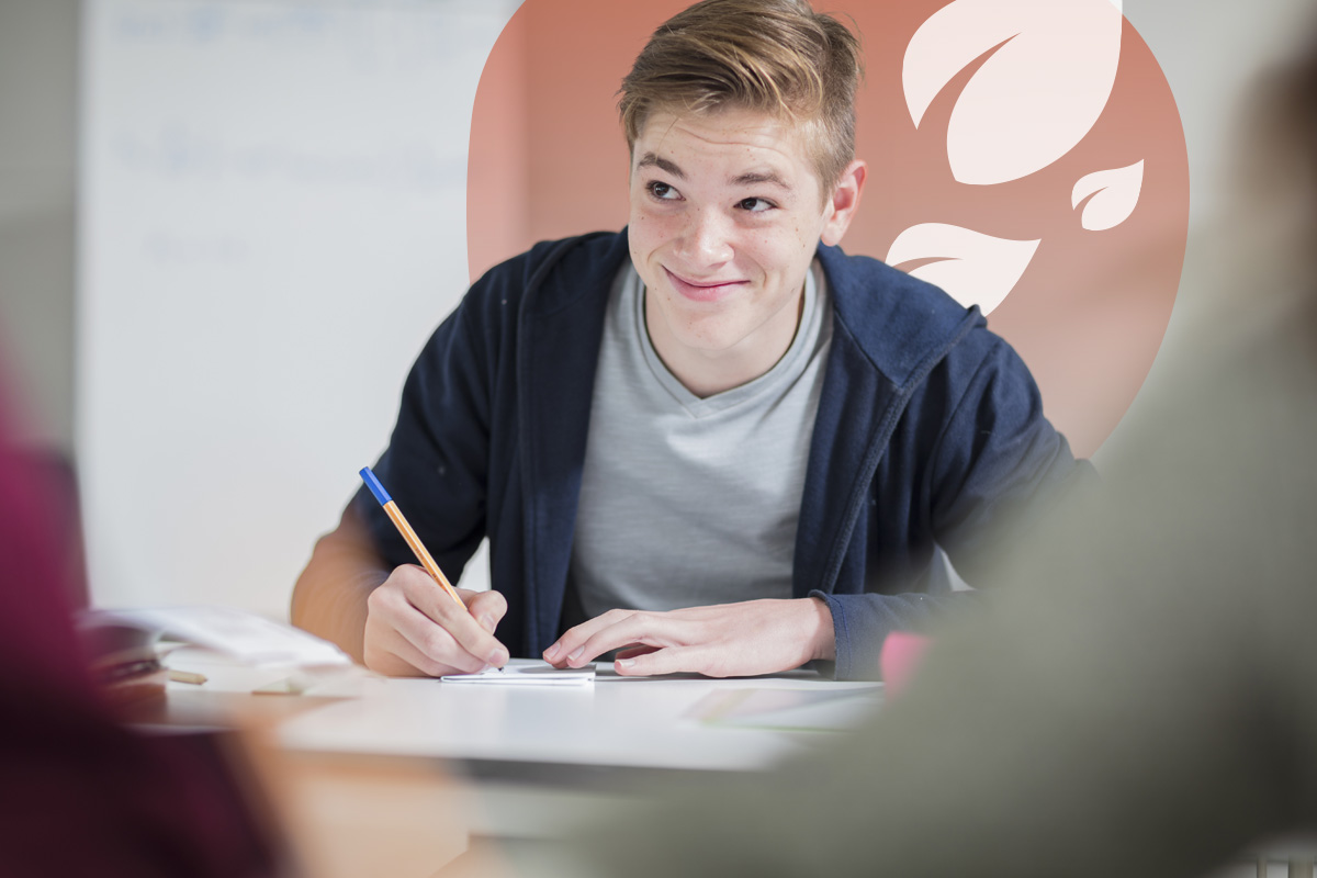 Teenage boy in casual clothing smiling while writing in a notebook during study.