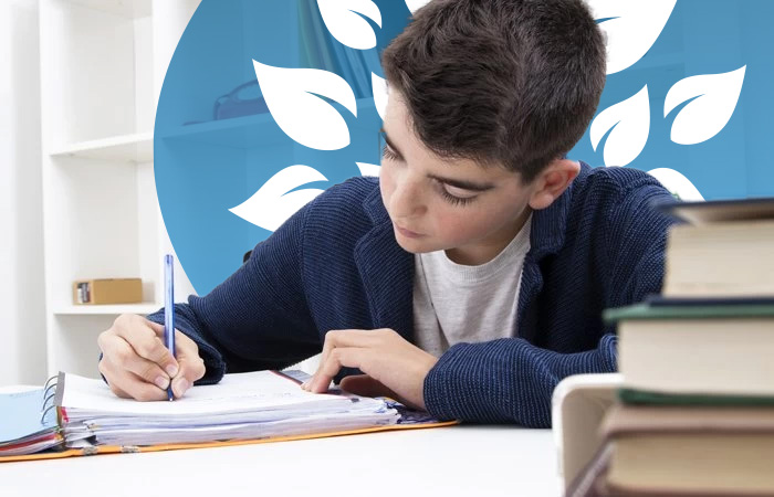A homeschooling young boy with short black hair writing in a notepad at a desk with books.