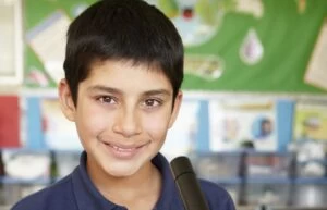 A close-up photograph of a Lower Secondary-age boy with short black hair smiling at the camera.