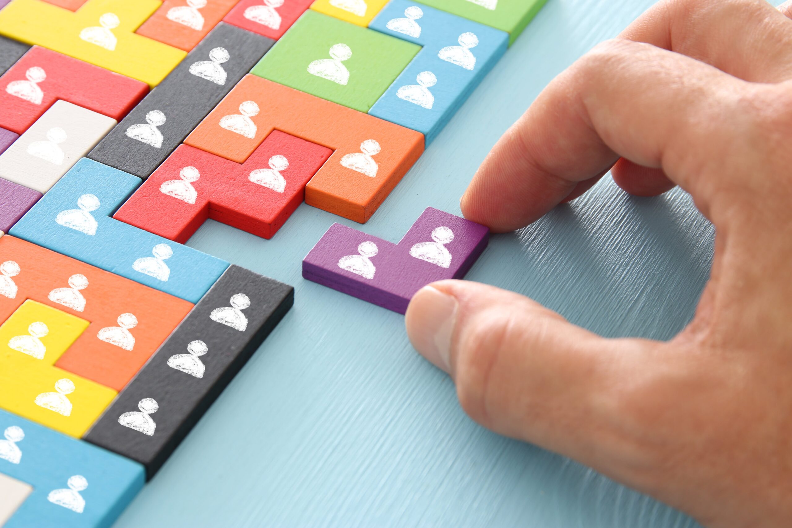 Hand placing a purple puzzle piece among colourful blocks, each marked with a white person icon