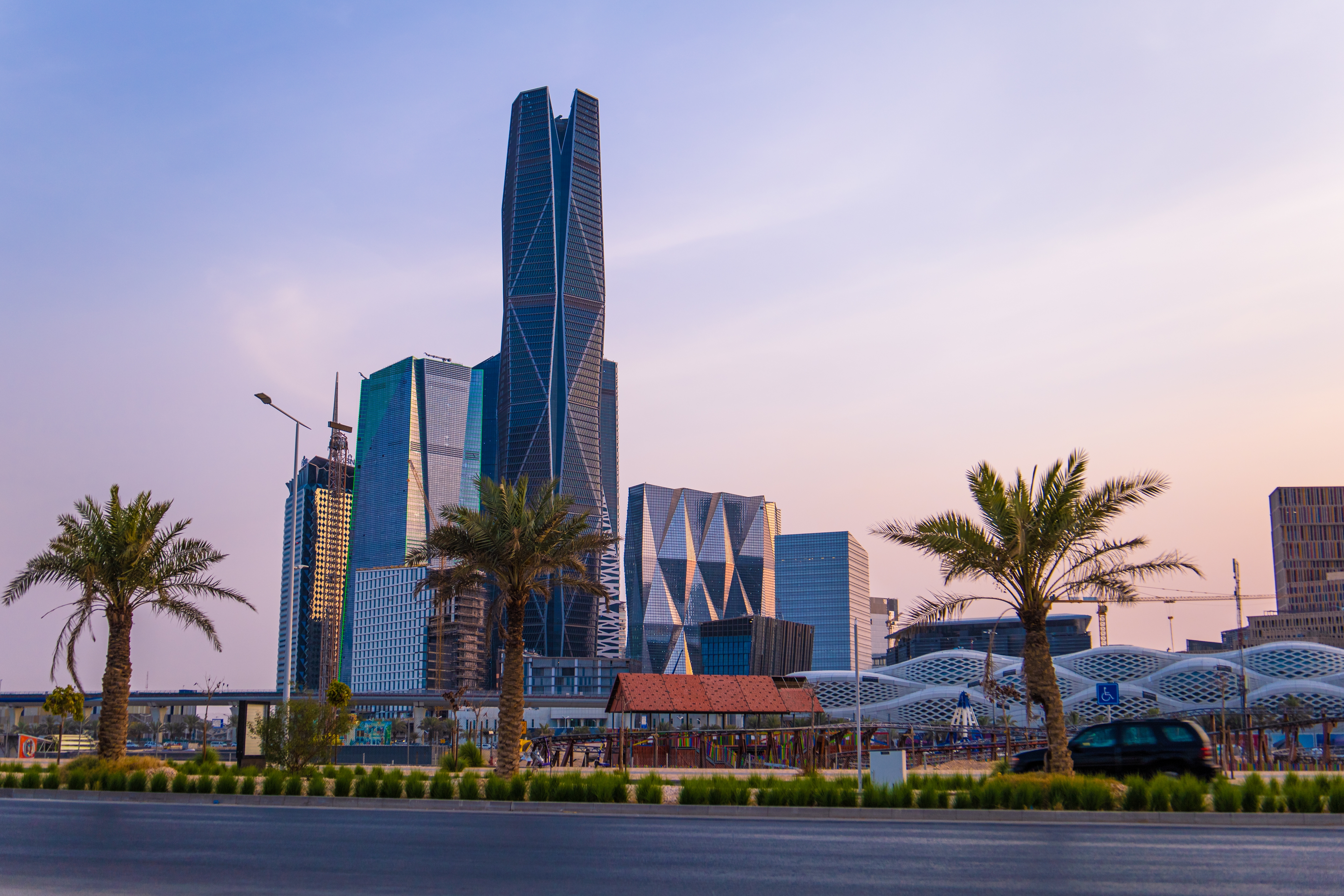 Modern skyscrapers in Riyadh, Saudi Arabia, seen from a palm-lined boulevard at sunset