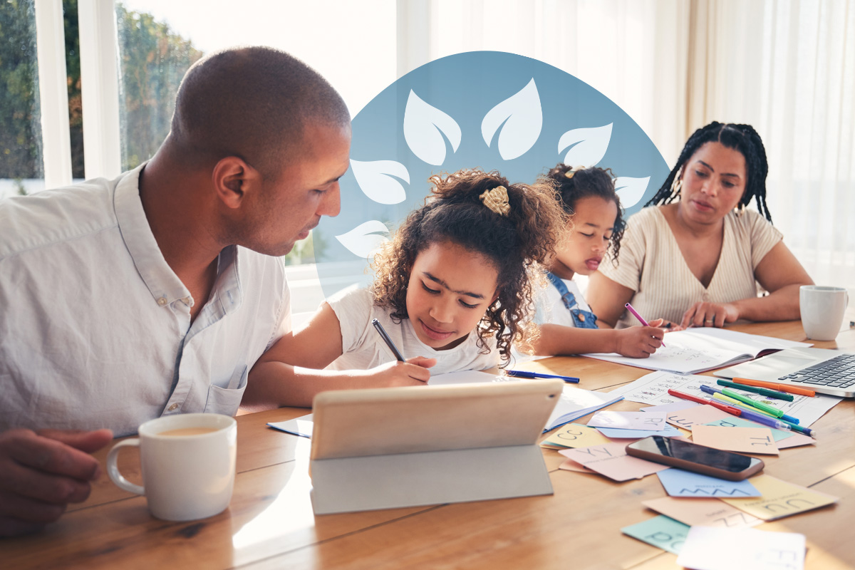 Two adults assisting two children who are writing and using a tablet at a dining table filled with study materials.