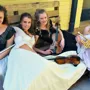 Four students in period costumes, holding musical instruments including a flute, violins and a trumpet.