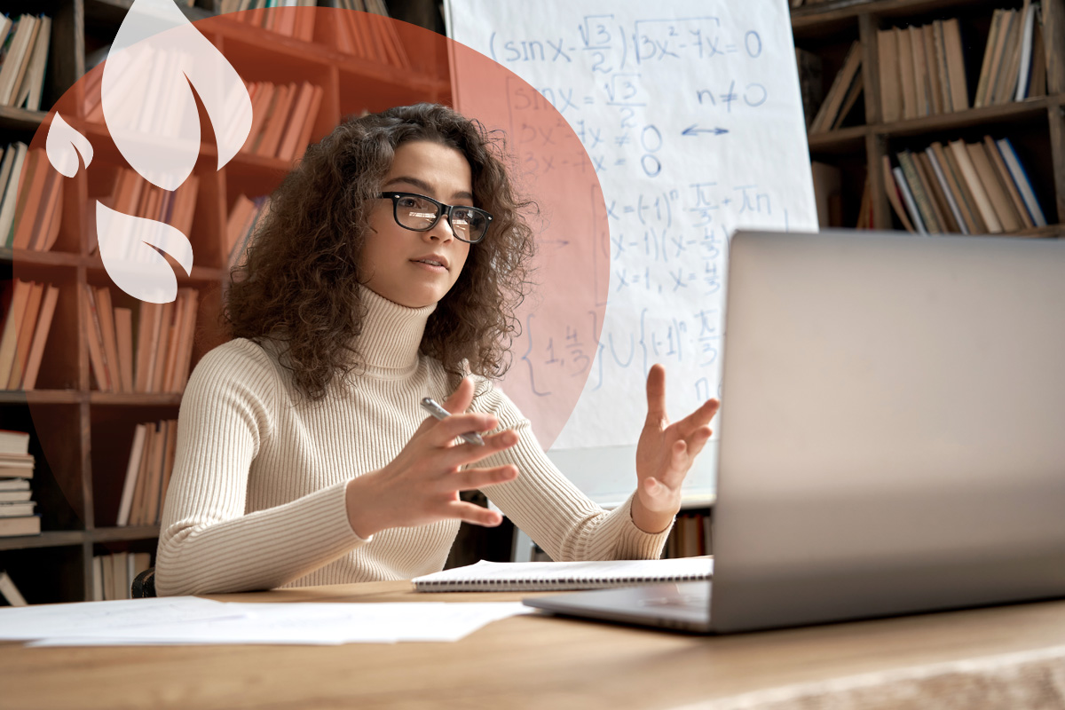 A specialist online tutor gestures towards her laptop as she teaches a complex maths lesson from her study.
