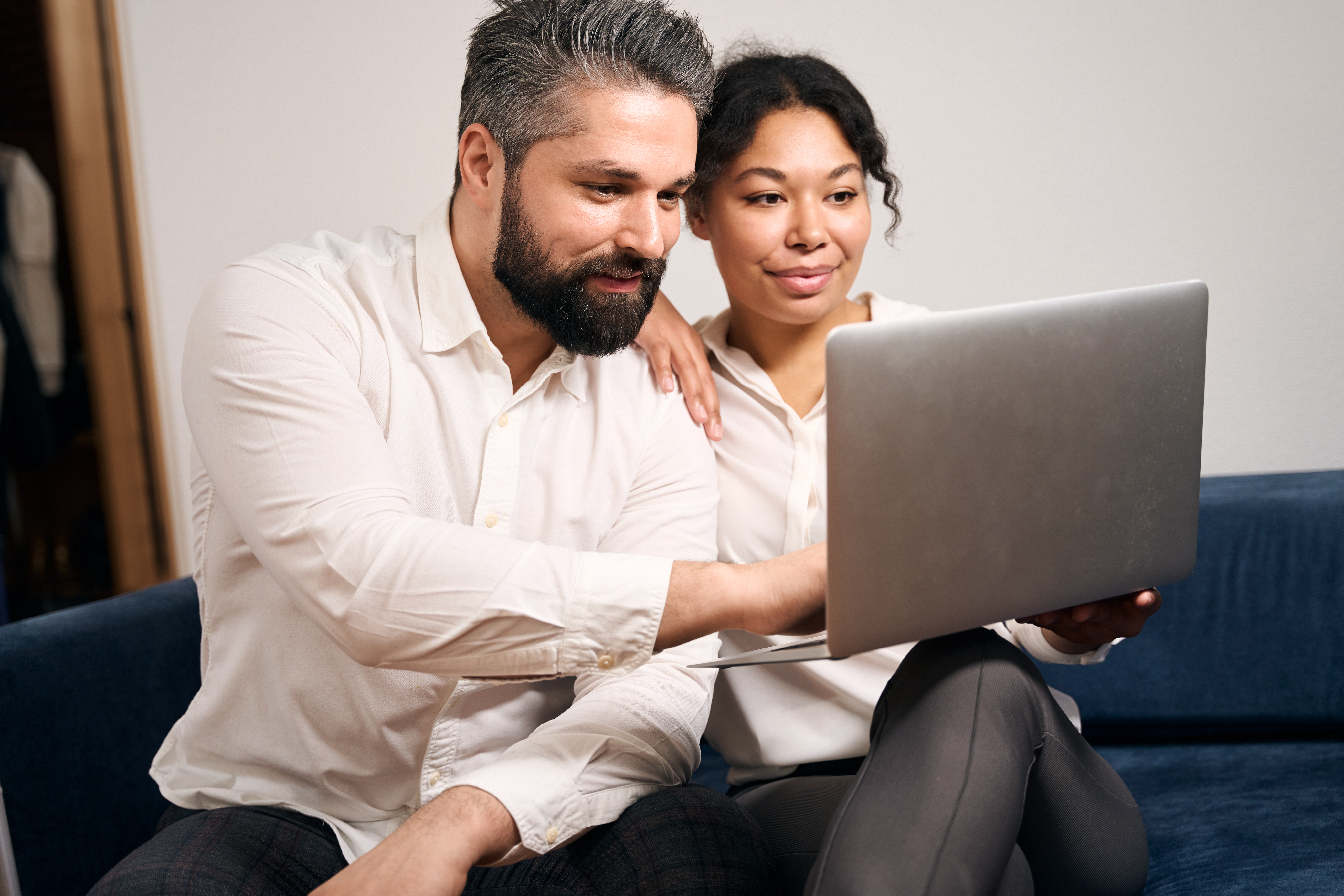 Couple seated closely on a sofa, attentively viewing a laptop screen in a relaxed home setting.