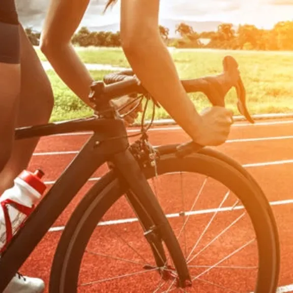 A close up image of a track cyclist riding on a track as the sun is starting to set.