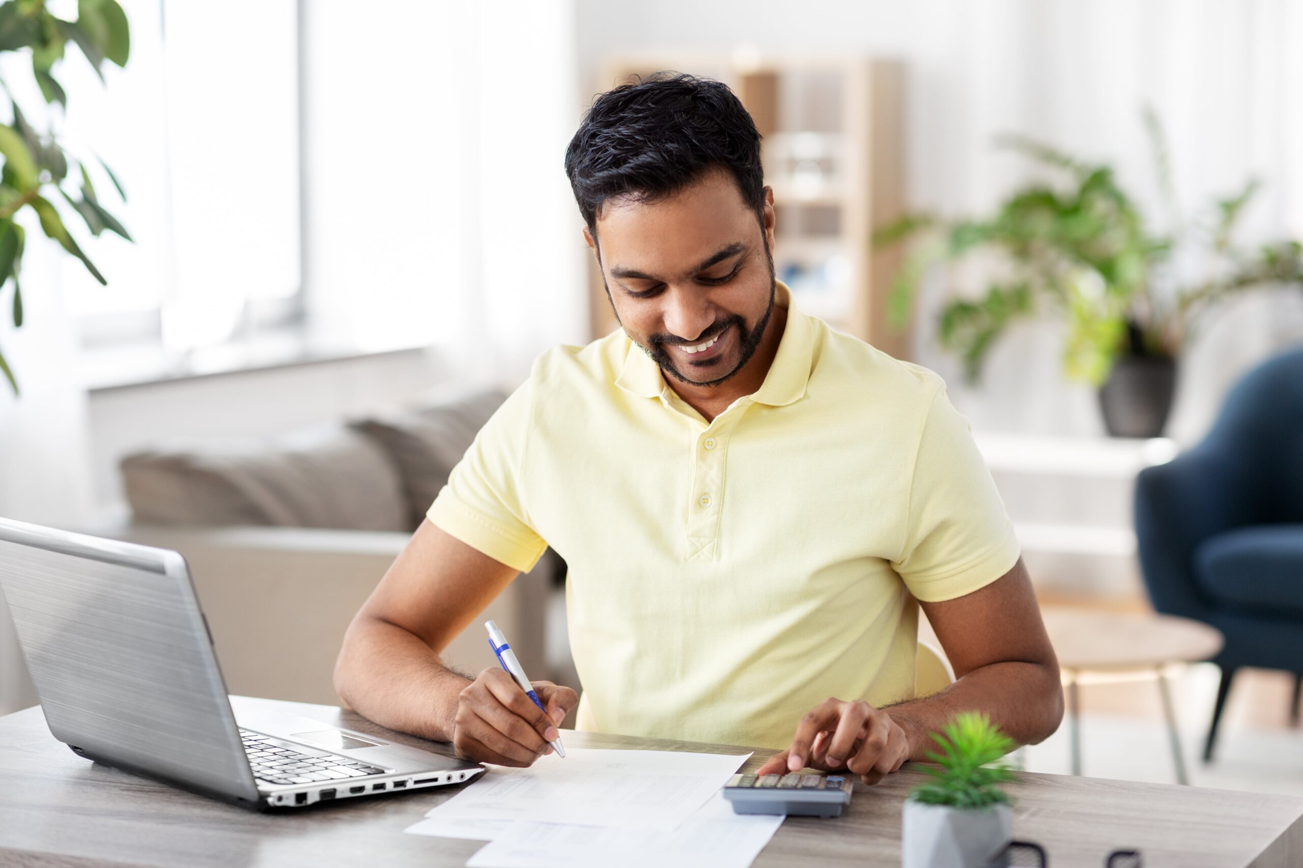 Man smiling while working on a laptop and with a calculator, possibly managing homeschool finances for his family in Riyadh.