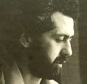 A close-up sepia photograph of John Coffey, who joined Wolsey Hall Oxford as Principal in 1987. John is looking down to the right. He has bushy black hair and a black beard and mustache.