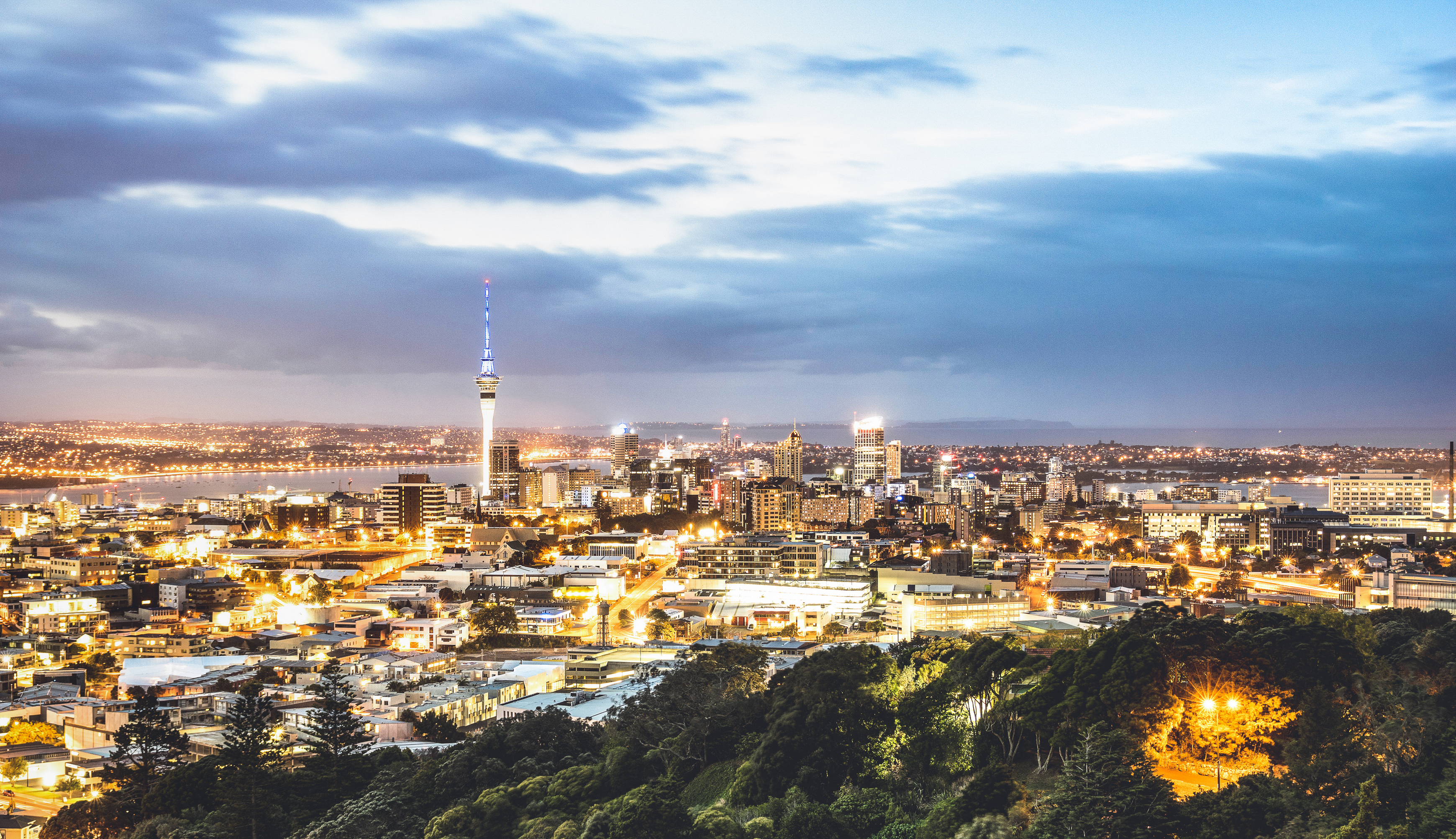 Auckland cityscape at dusk with Sky Tower lit up and reflections across the harbour
