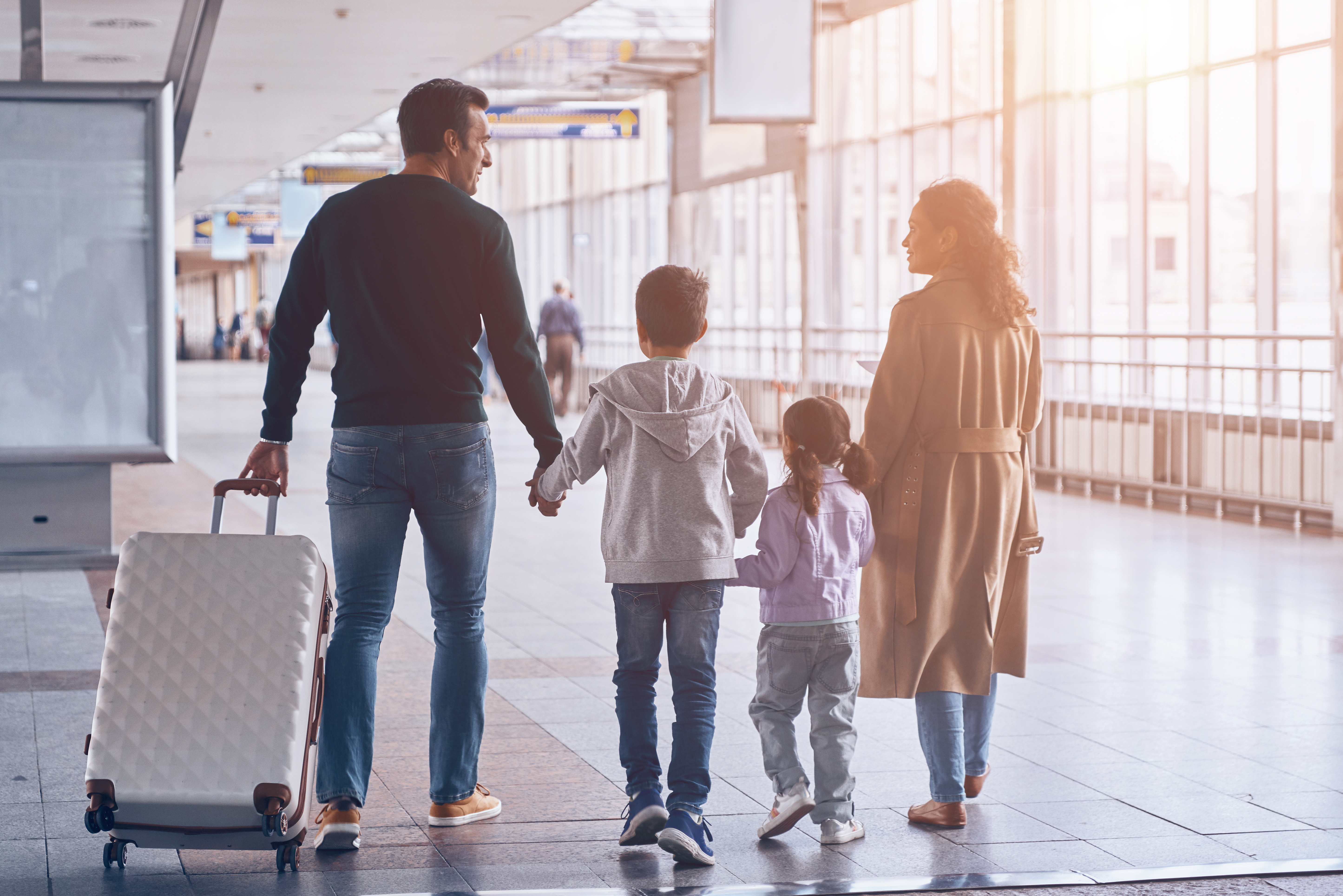 Family of four walking hand in hand through airport with travel bags