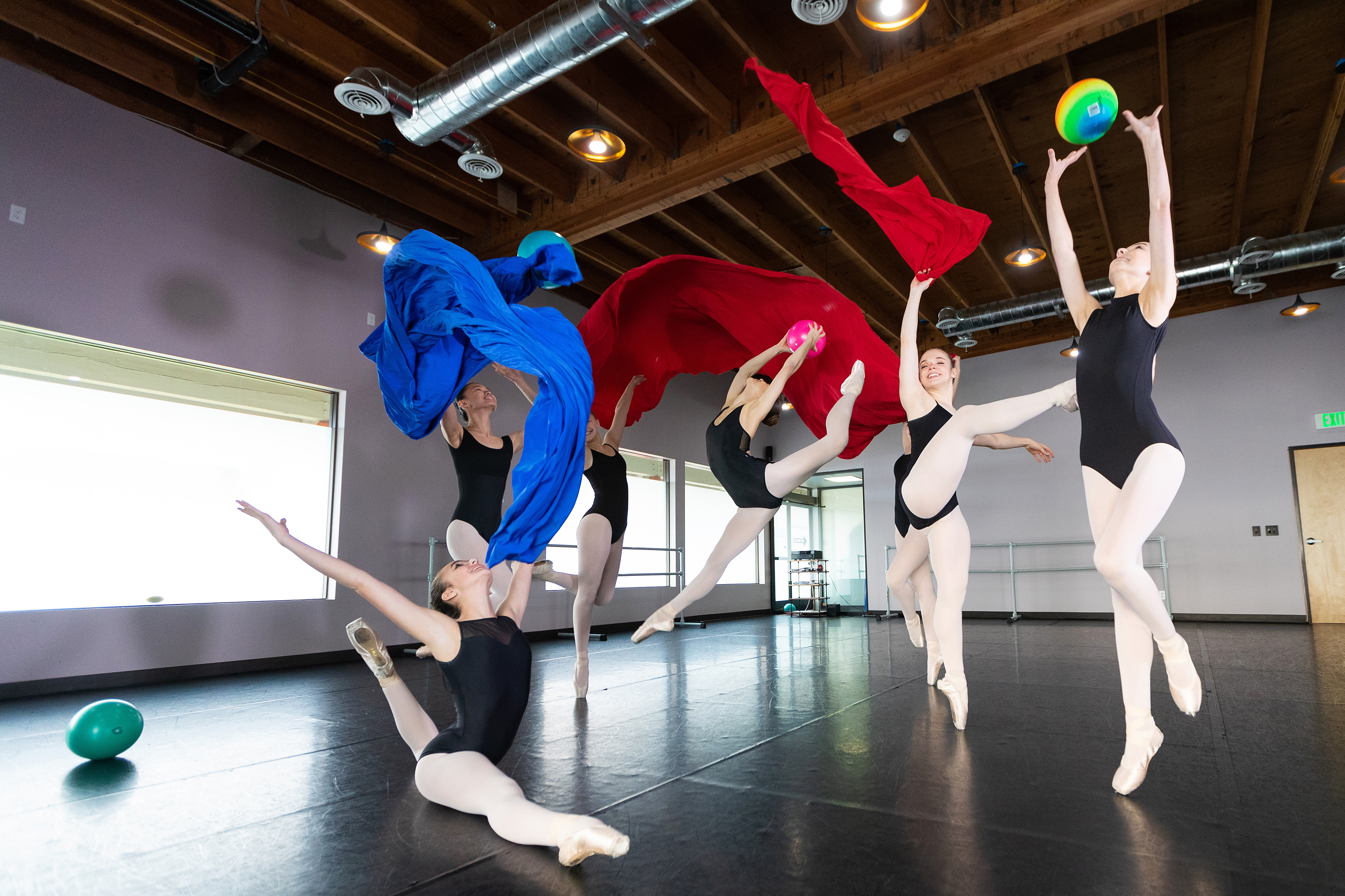 Ballet dancers mid-performance in studio with flowing red and blue fabric