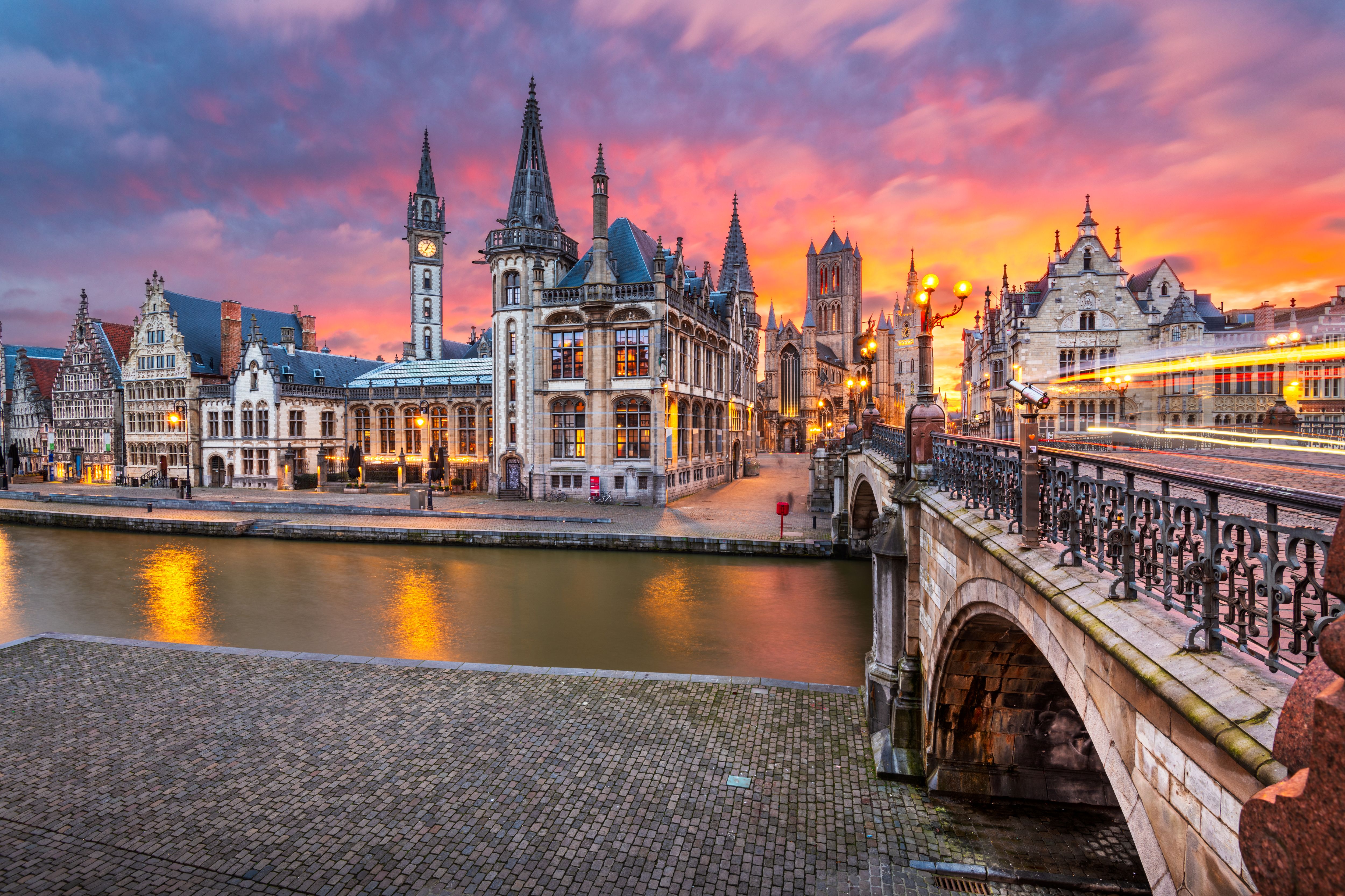 Historic buildings along a canal in Ghent at sunset with glowing streetlights and reflections