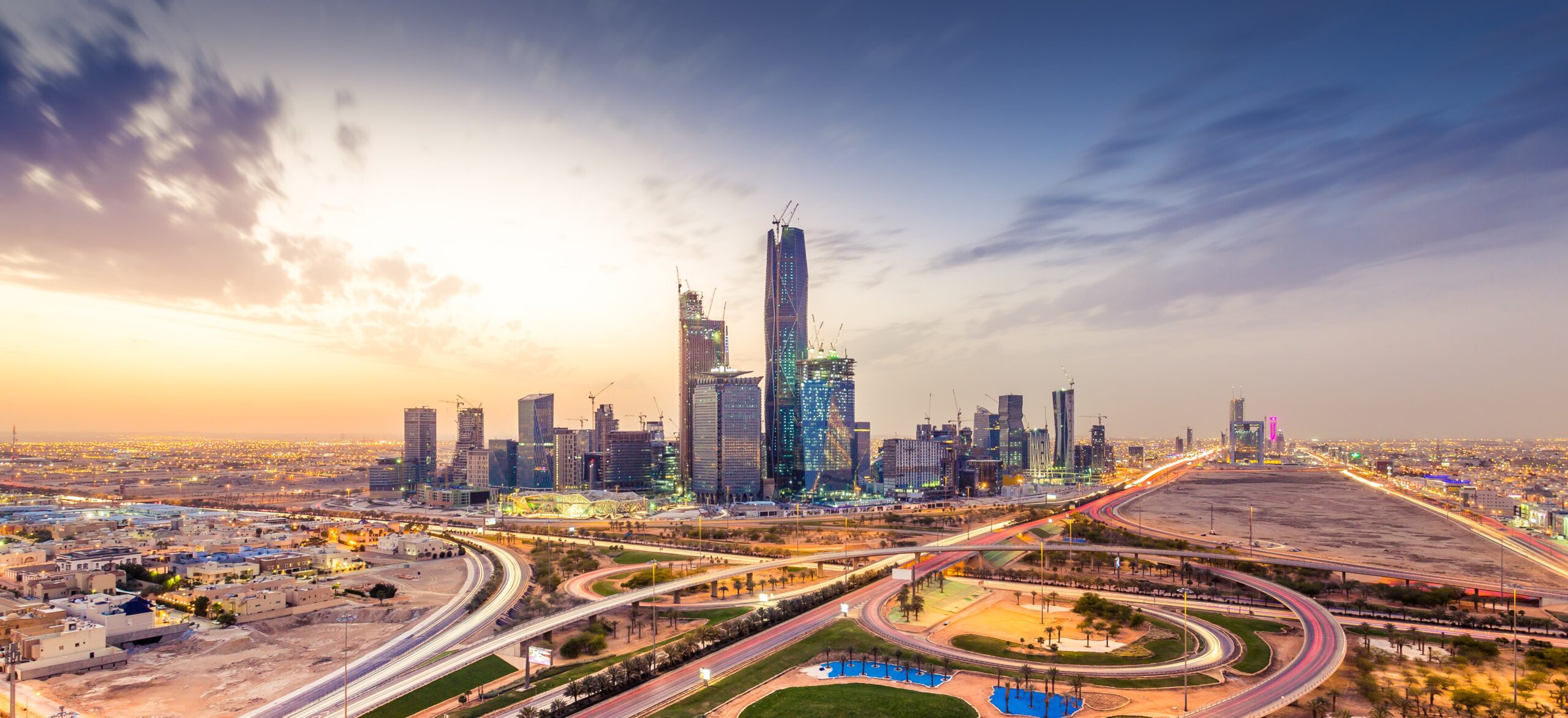 Expansive evening view of the Riyadh, Saudi Arabia skyline with illuminated skyscrapers and city lights.
