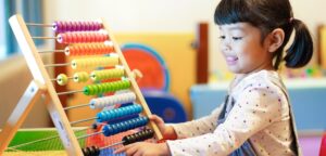 A photograph of a Primary-age girl with black hair playing with a large abacus.