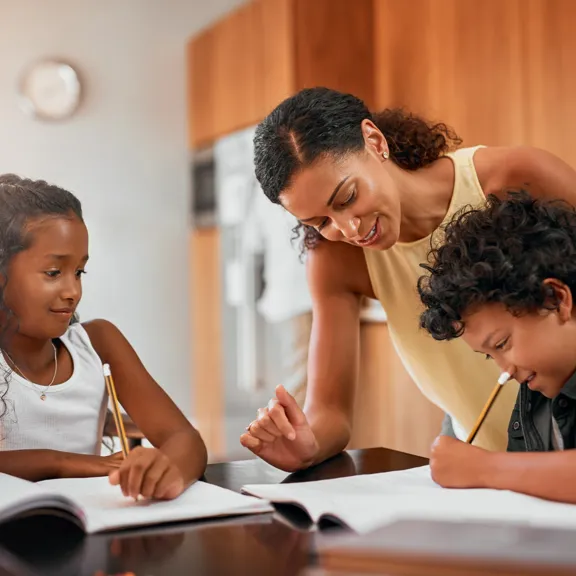 Smiling parent helping two children with their studies at the kitchen table.