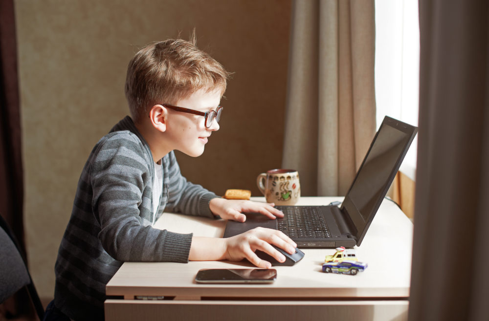 Young boy wearing glasses engaged in an interactive learning session on his laptop during homeschooling.