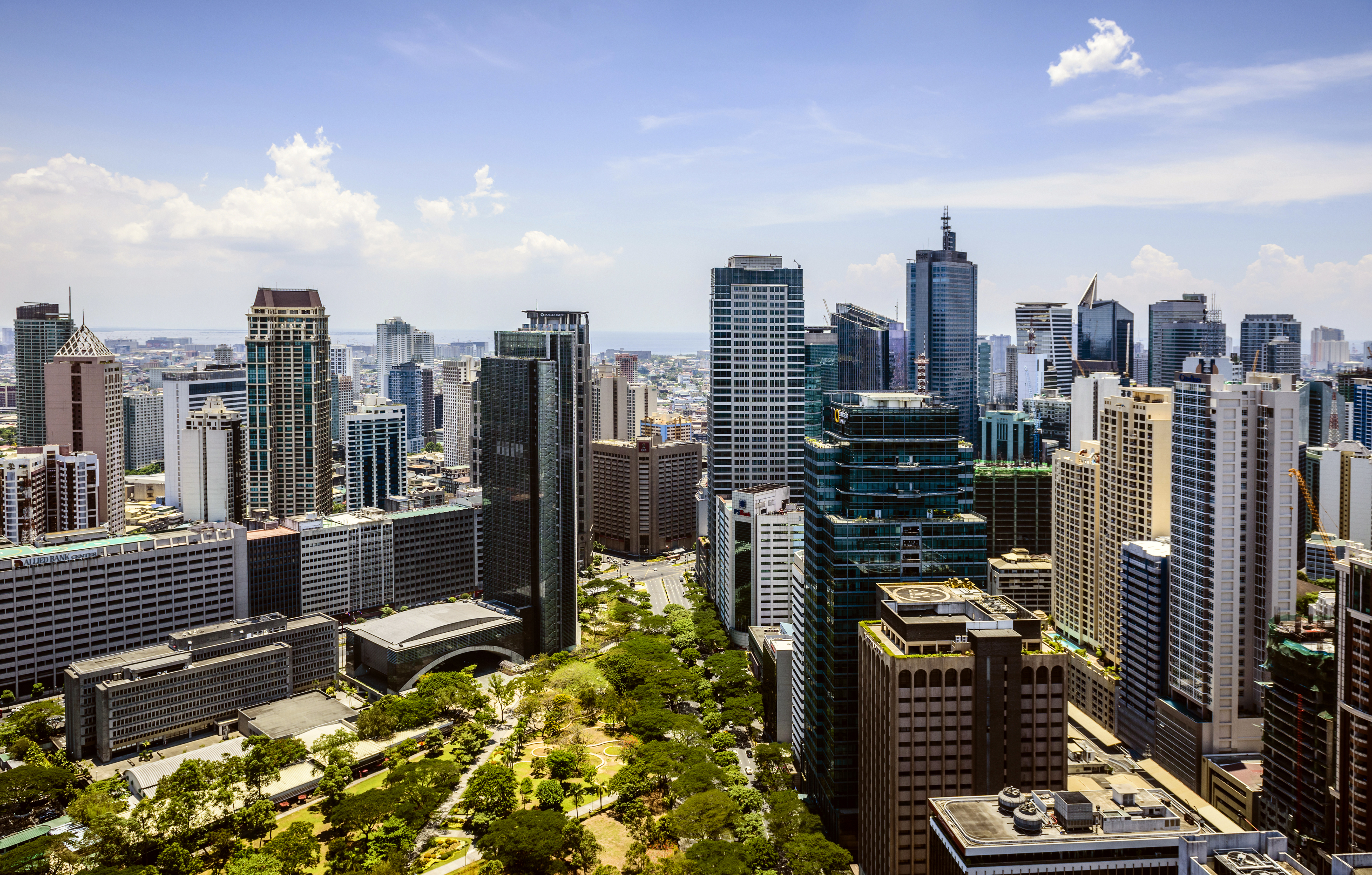 Manila skyline with high-rise buildings and tree-lined roads under a bright blue sky