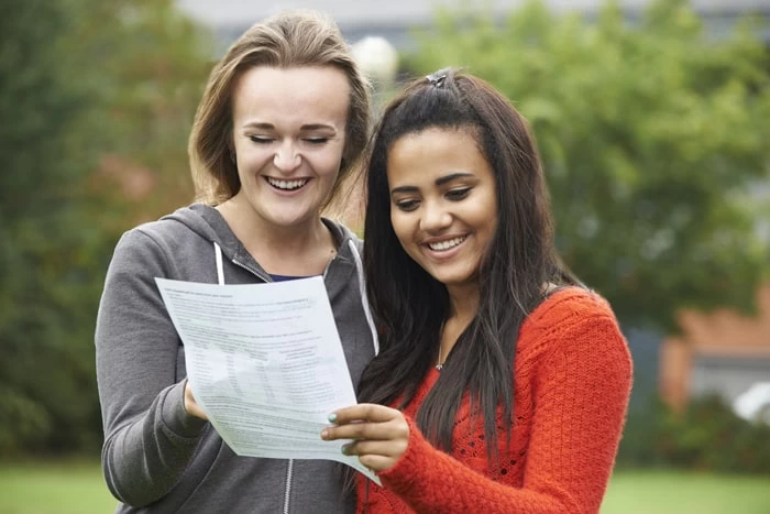 Two homeschooling female students are holding an exam results certificate and smiling.