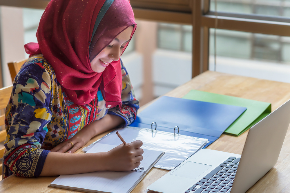 Student diligently working on her studies with a notebook and computer, representing effective homeschooling in Jeddah.