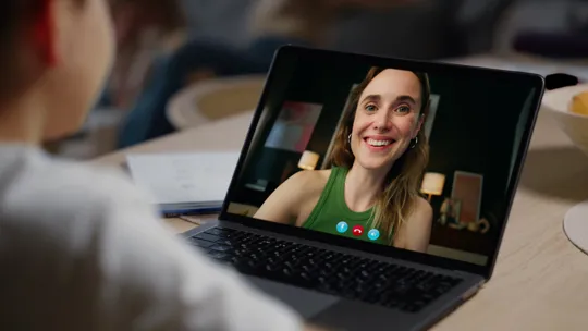 Close-up of a laptop screen showing a smiling tutor on a video call with a student.