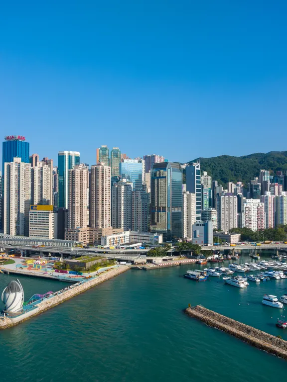Modern high-rise skyline of Hong Kong overlooking Victoria Harbour and docked boats.