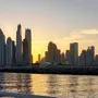 A panoramic view of a city skyline at sunset, with tall buildings reflecting in the water of a harbour or bay.