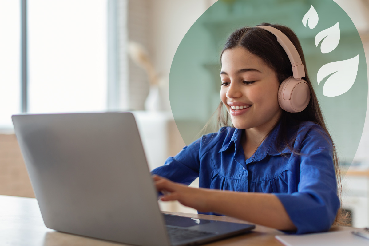 A young student wearing pink headphones, smiling and looking at a laptop while typing.