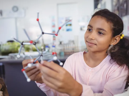 School-aged girl examining a molecular model in a science classroom.