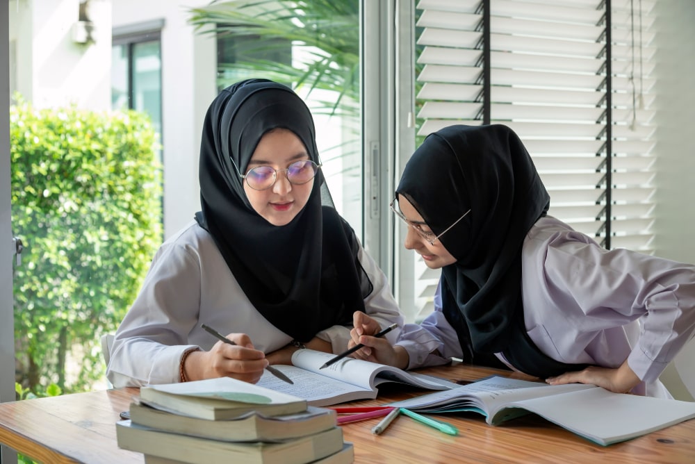 Focused learning in a Sharjah homeschooling environment: two students collaborate on their studies with books and notes.