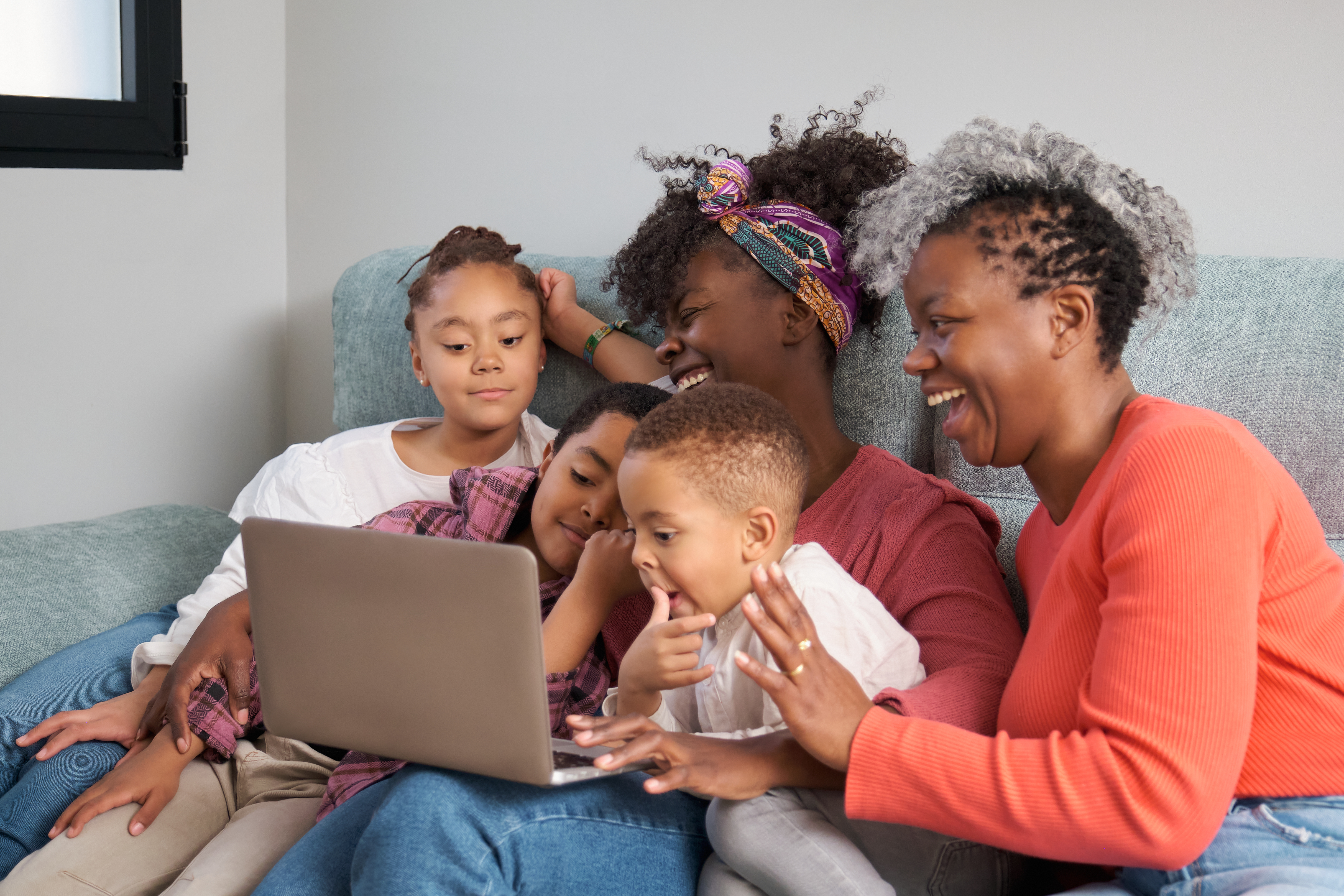 Family of five sharing a moment of learning and laughter together on the sofa with a laptop.