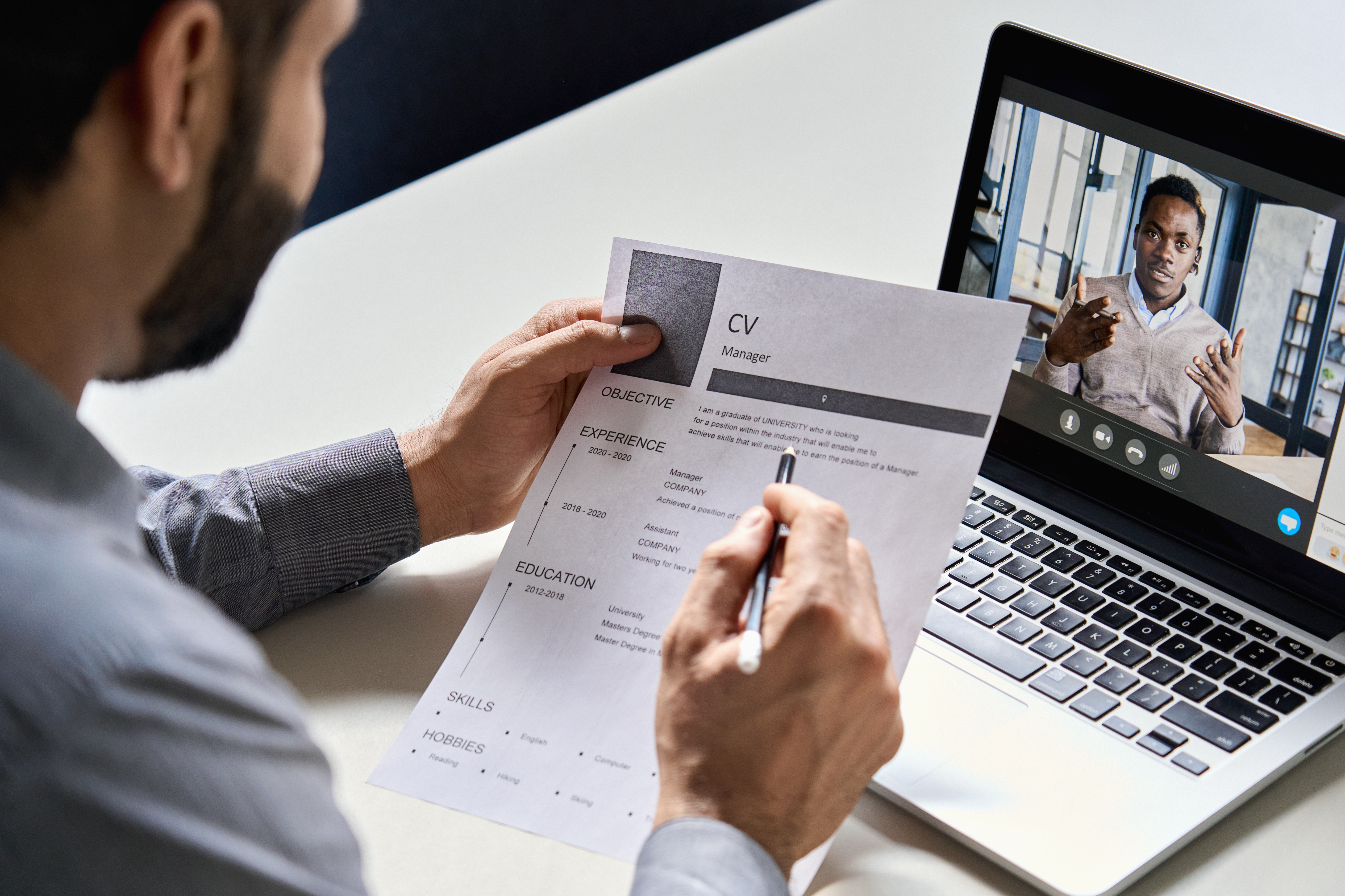 A hiring manager reviews a CV during a remote video interview with a job applicant.