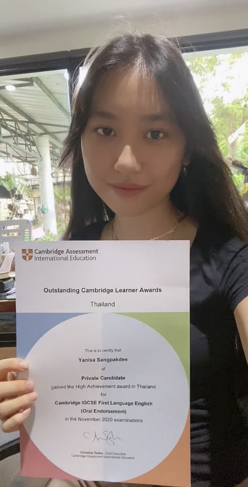 Wolsey Hall Oxford student Genie smiles at the camera holding her Outstanding Cambridge Learner Award certificate.