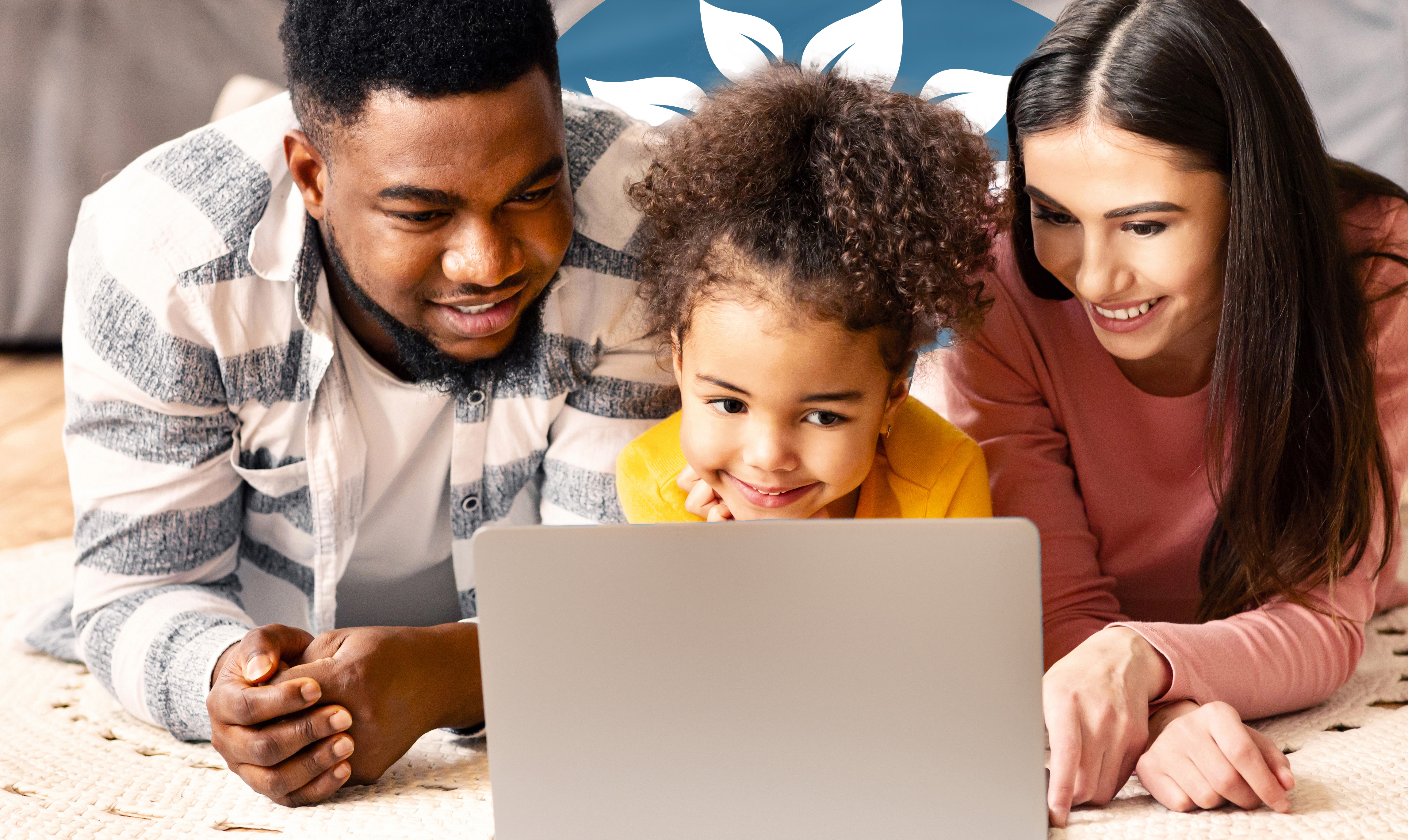 A family lying on the floor, smiling and looking at a laptop together, suggesting engaging online learning or family activities.