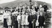 An old black and white photograph of a group of schoolchildren standing together and looking at the camera.