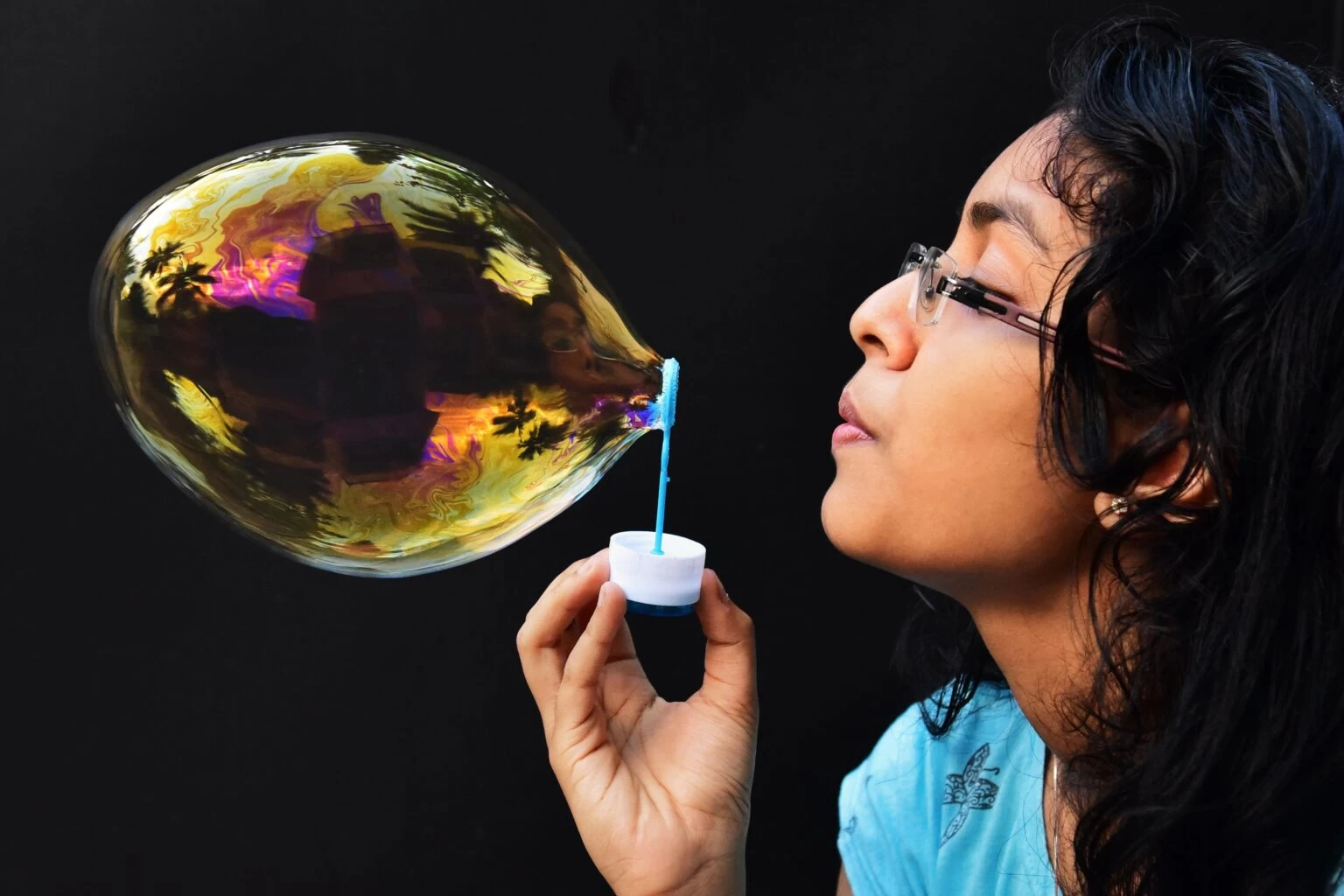 A girl blowing a bubble through a plastic hoop. 